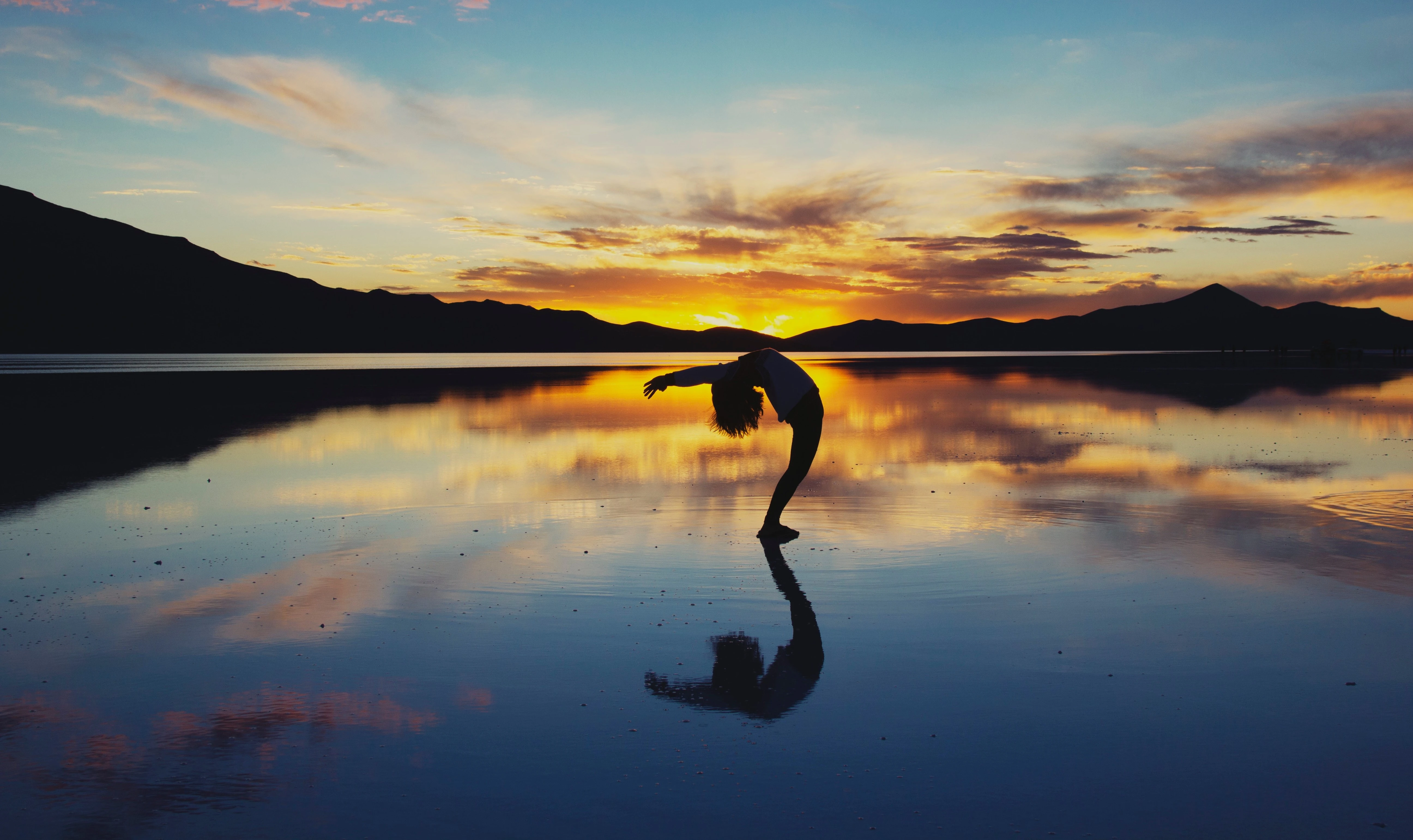 Femme faisant une posture sur l'eau avec un coucher de soleil en fond